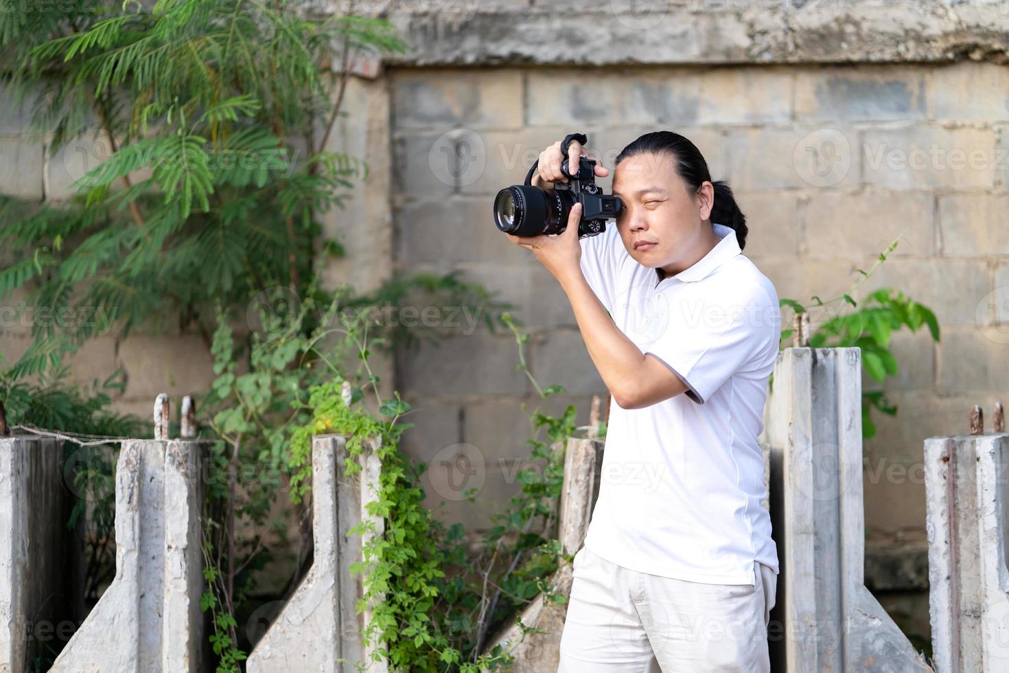 Professional Asian Chinese - Thai Camera man posture and focus in viewfinder and LED screen on mirrorless camera medium format in construction concrete area. photo