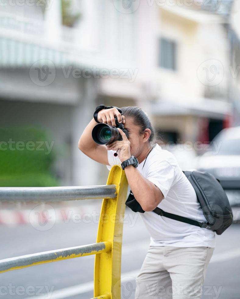 el camarógrafo profesional asiático se enfoca en la imagen con su cámara sin espejo al lado del campo al aire libre de la calle. foto