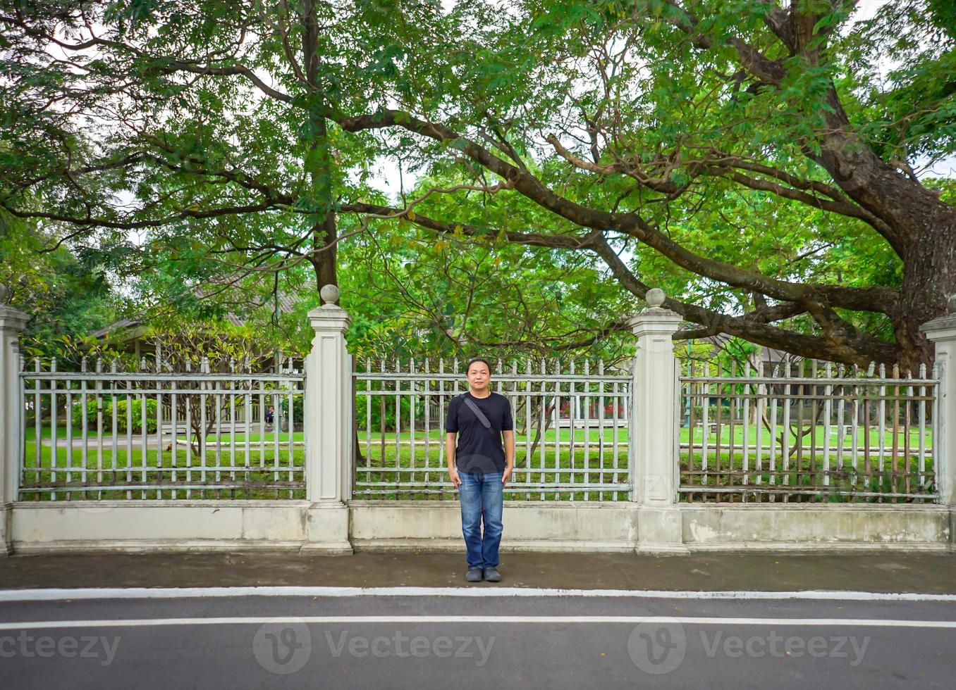 una camiseta negra asiática está parada frente a una valla blanca vintage al lado de la carretera por la tarde. foto