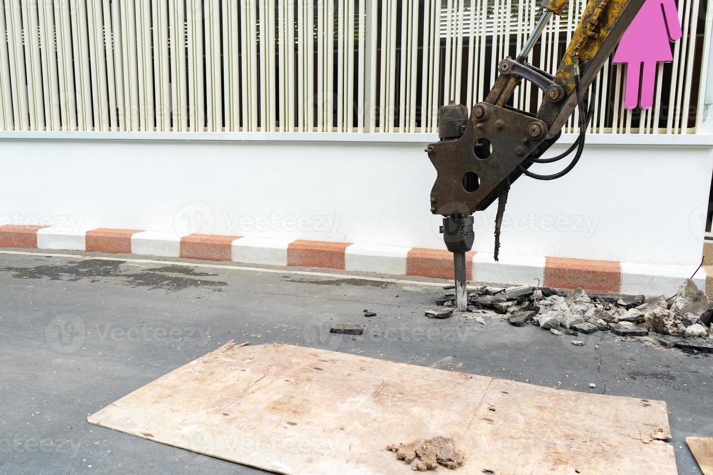 Pneumatic drill demolish machine Backhoe is dicking concrete road beside the wall. photo