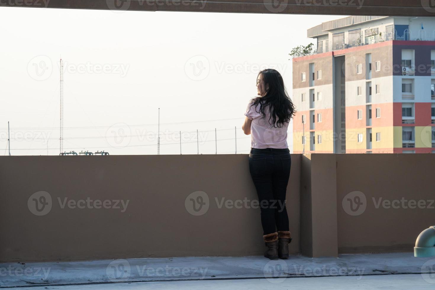 Asian female teen stands backside in front of city view at rooftop of the building photo