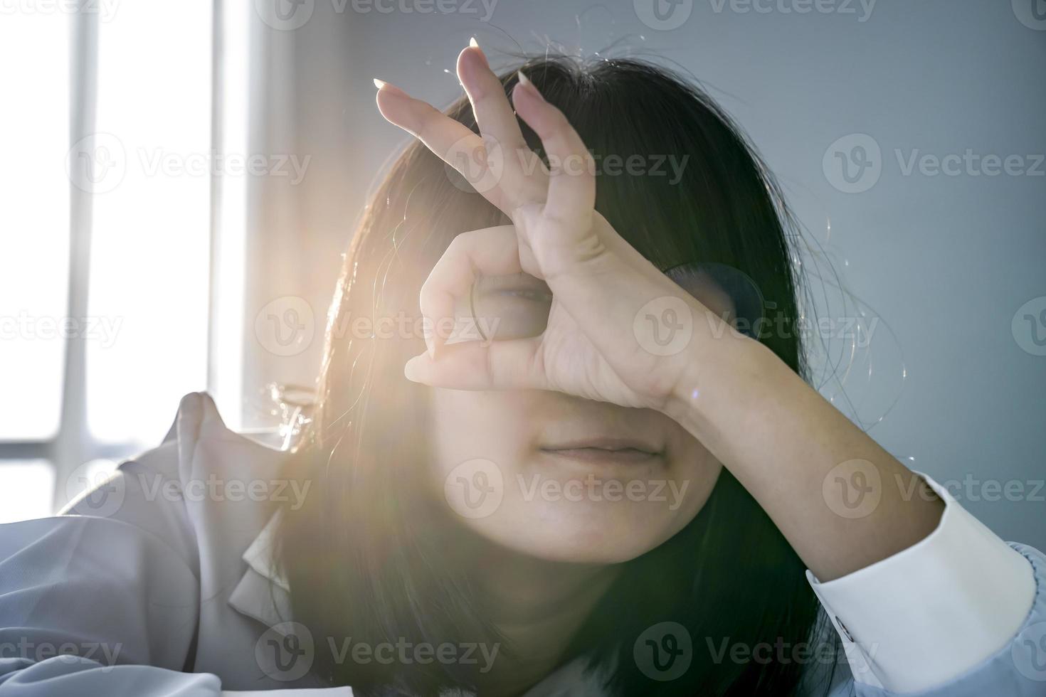 Young Glassese Asian Chinese - Thai girl is smiling happy doing OK sign with raising hand up on her eye looking through to camera. photo