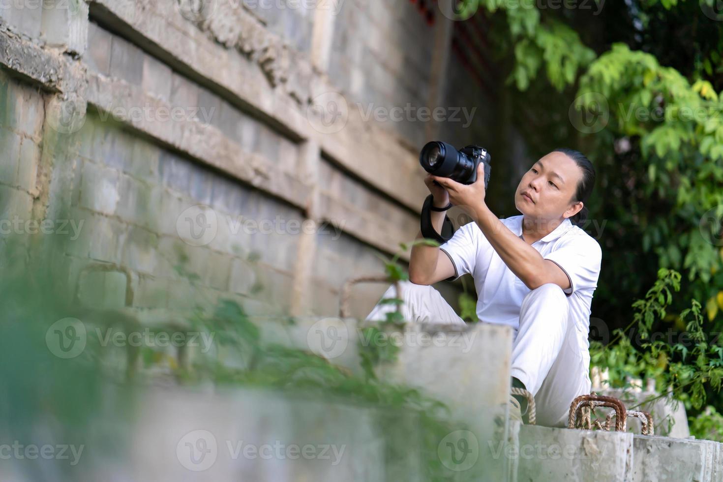 Professional Asian Chinese - Thai Camera man posture and focus in viewfinder and LED screen on mirrorless camera medium format in construction concrete area. photo