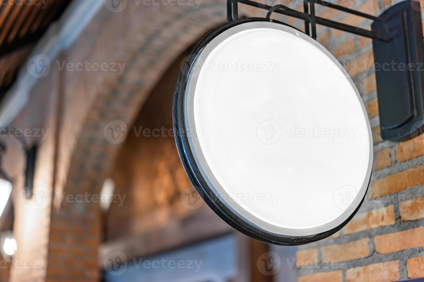 la caja de luz blanca del círculo ha colgado en la pared frente al poste de ladrillo en un centro comercial comunitario de ambiente de tungsteno. foto