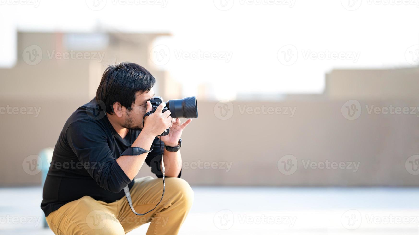 Asian Professional Camera man looks in to camera viewfinder and focus on the view for take a photo at rooftop outdoor field.