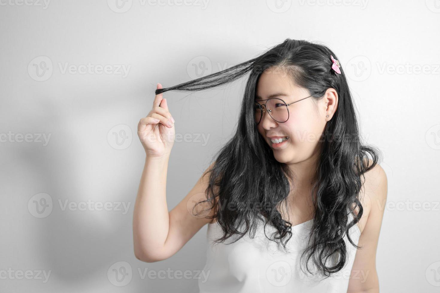 una chica tímida asiática feliz y sonríe jugando con su cabello en un estudio de fondo blanco claro. foto