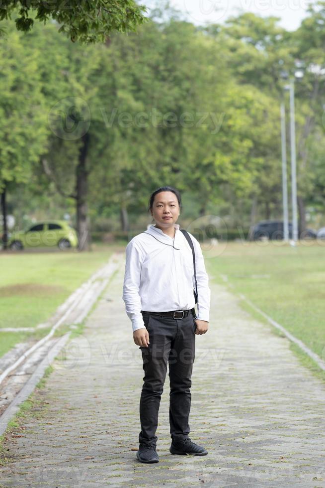 Asian freelance long hair man standing and posting on the walk way in the garden outdoor field with his camera beside him. photo