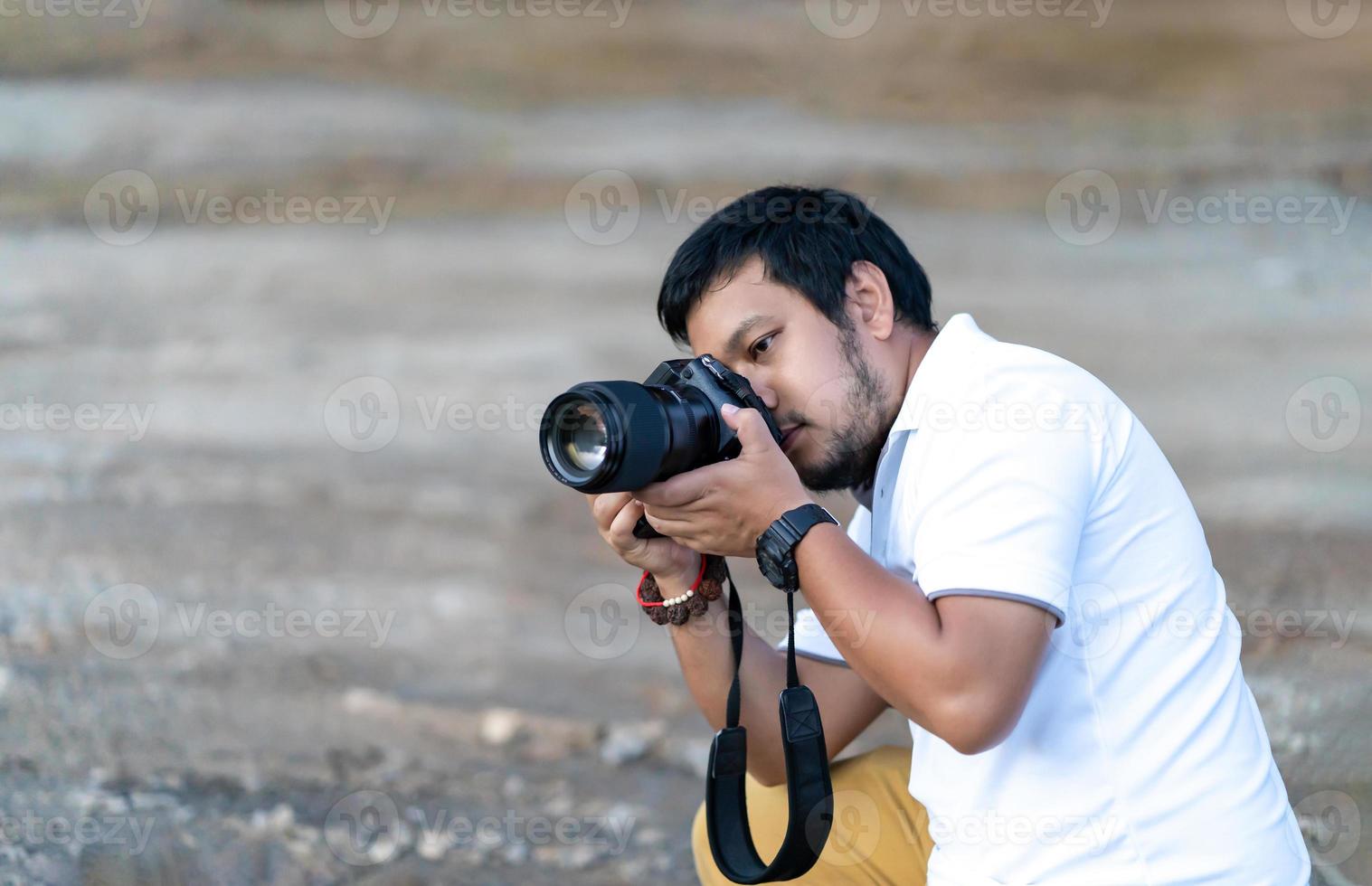 Professional Asian beard - mustache Camera man posture and focus in viewfinder and LED screen on mirrorless camera medium format in construction concrete area. photo