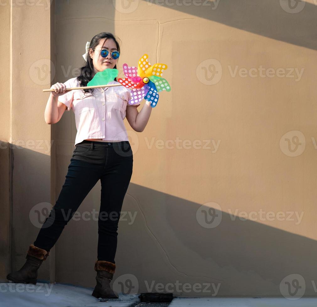 Asian woman posts and play Windmill Toy colourful rainbow colour on the building rooftop in sunset time. photo