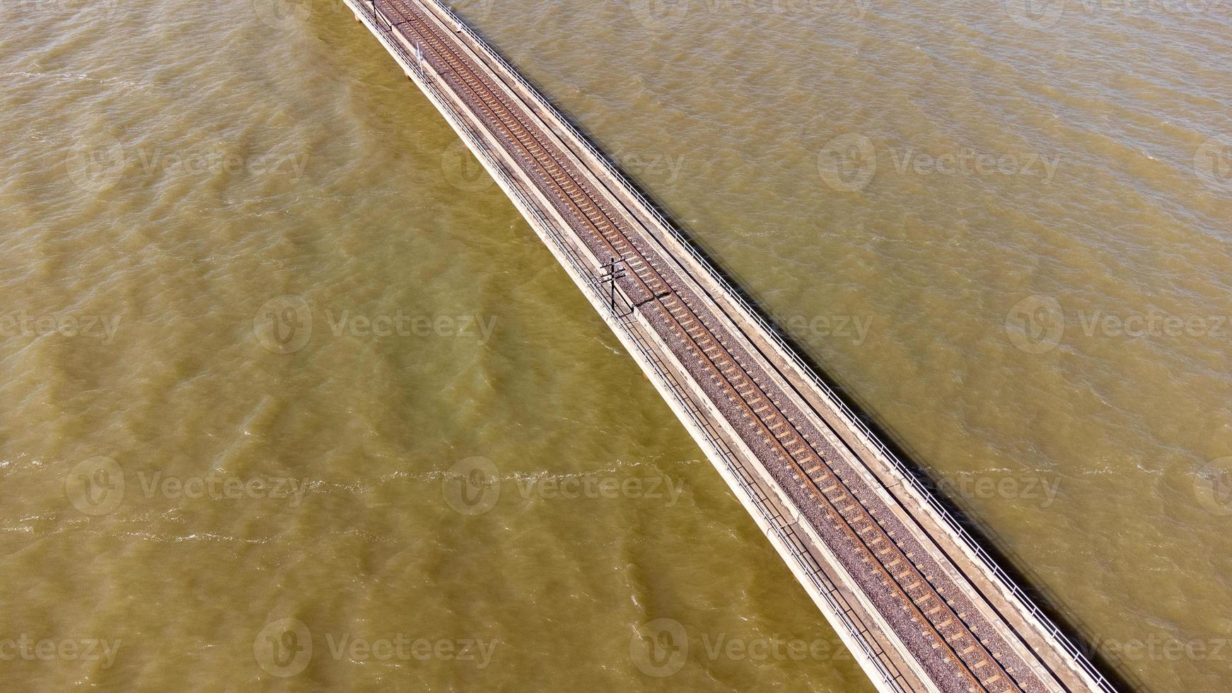 vista aérea de un increíble tren de viaje estacionado en un puente ferroviario flotante sobre el agua del lago en la presa pa sak jolasid con cielo azul en lopburi, tailandia. foto