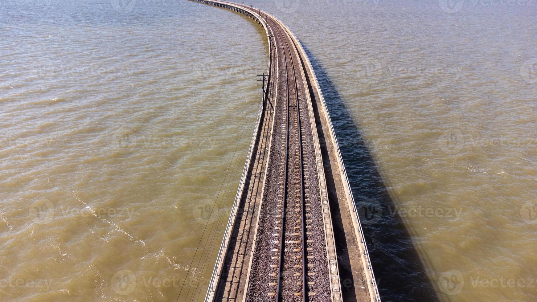 Aerial view of an amazing travel train parked on a floating railway bridge over the water of the lake in Pa Sak Jolasid dam with blue sky at Lopburi, Thailand. photo