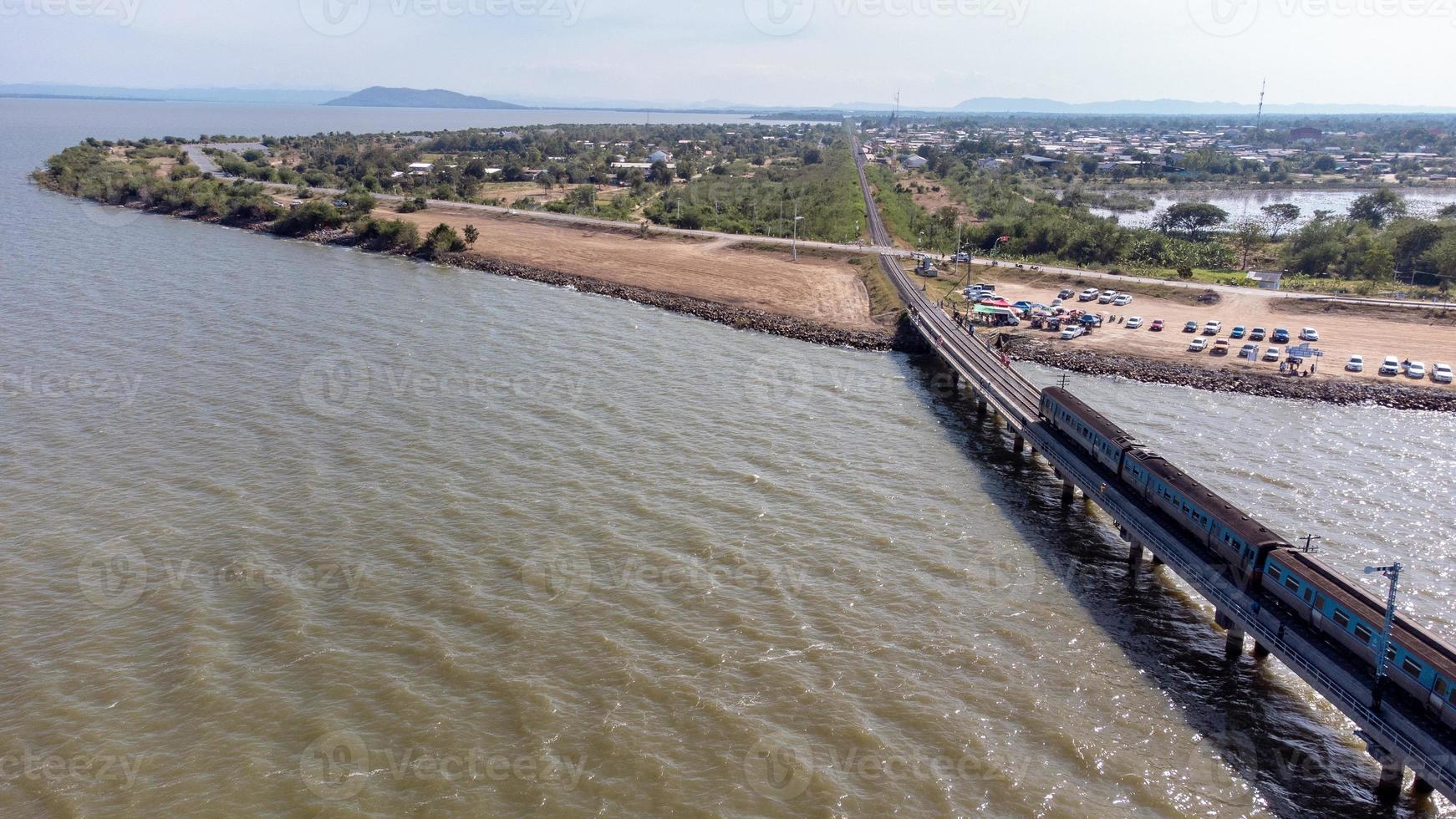 vista aérea de un increíble tren de viaje estacionado en un puente ferroviario flotante sobre el agua del lago en la presa pa sak jolasid con cielo azul en lopburi, tailandia. foto