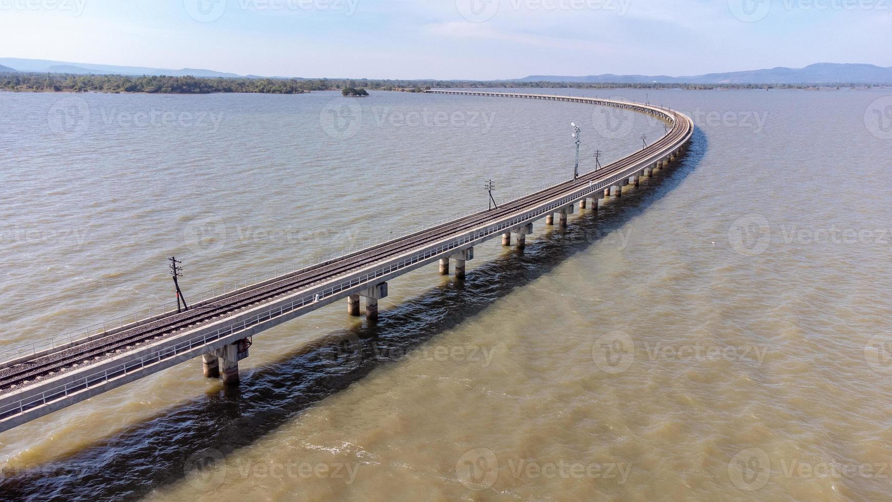 Aerial view of an amazing travel train parked on a floating railway bridge over the water of the lake in Pa Sak Jolasid dam with blue sky at Lopburi, Thailand. photo