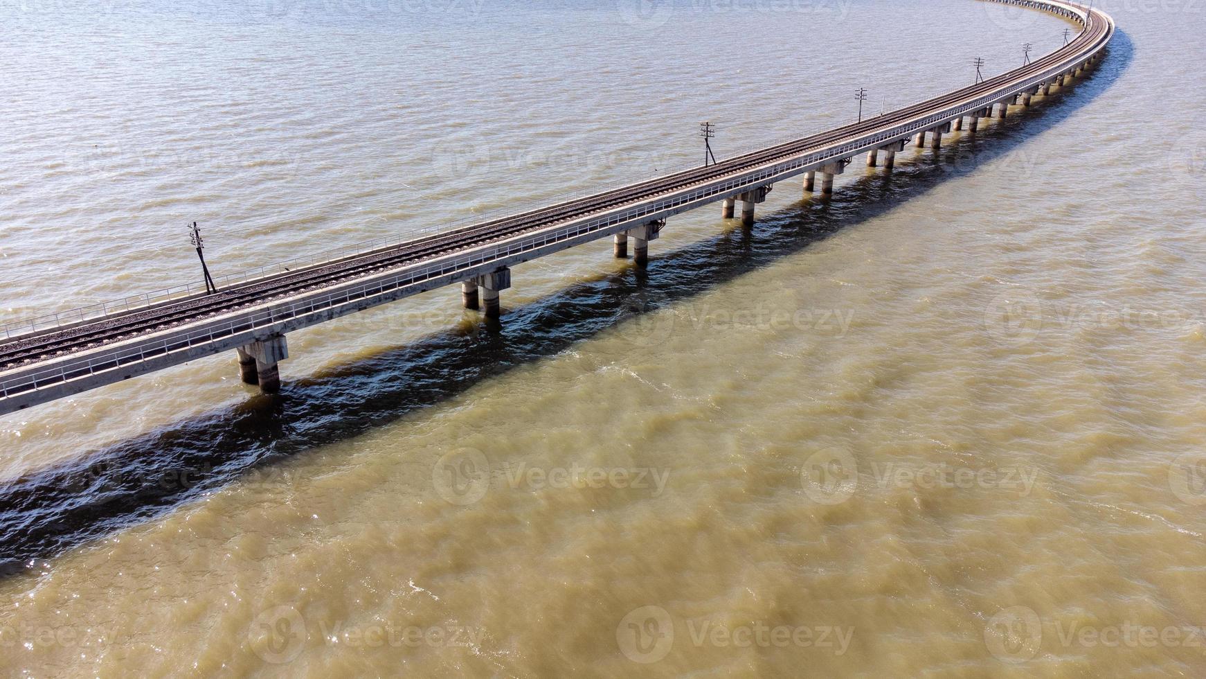 vista aérea de un increíble tren de viaje estacionado en un puente ferroviario flotante sobre el agua del lago en la presa pa sak jolasid con cielo azul en lopburi, tailandia. foto