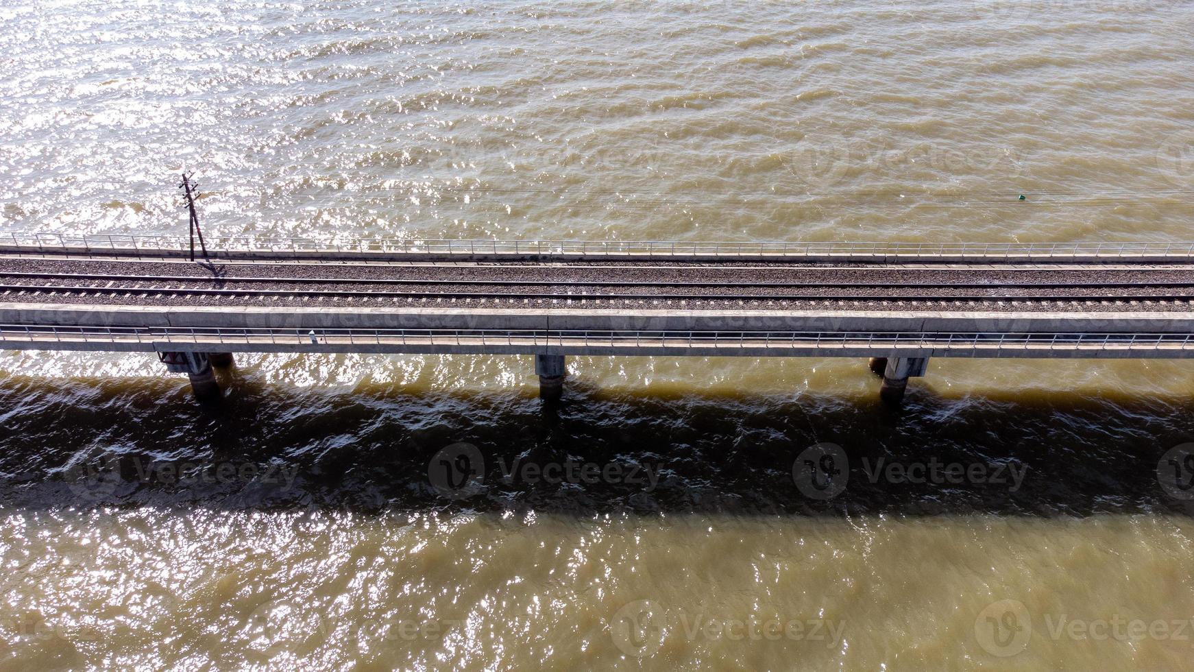 Aerial view of an amazing travel train parked on a floating railway bridge over the water of the lake in Pa Sak Jolasid dam with blue sky at Lopburi, Thailand. photo