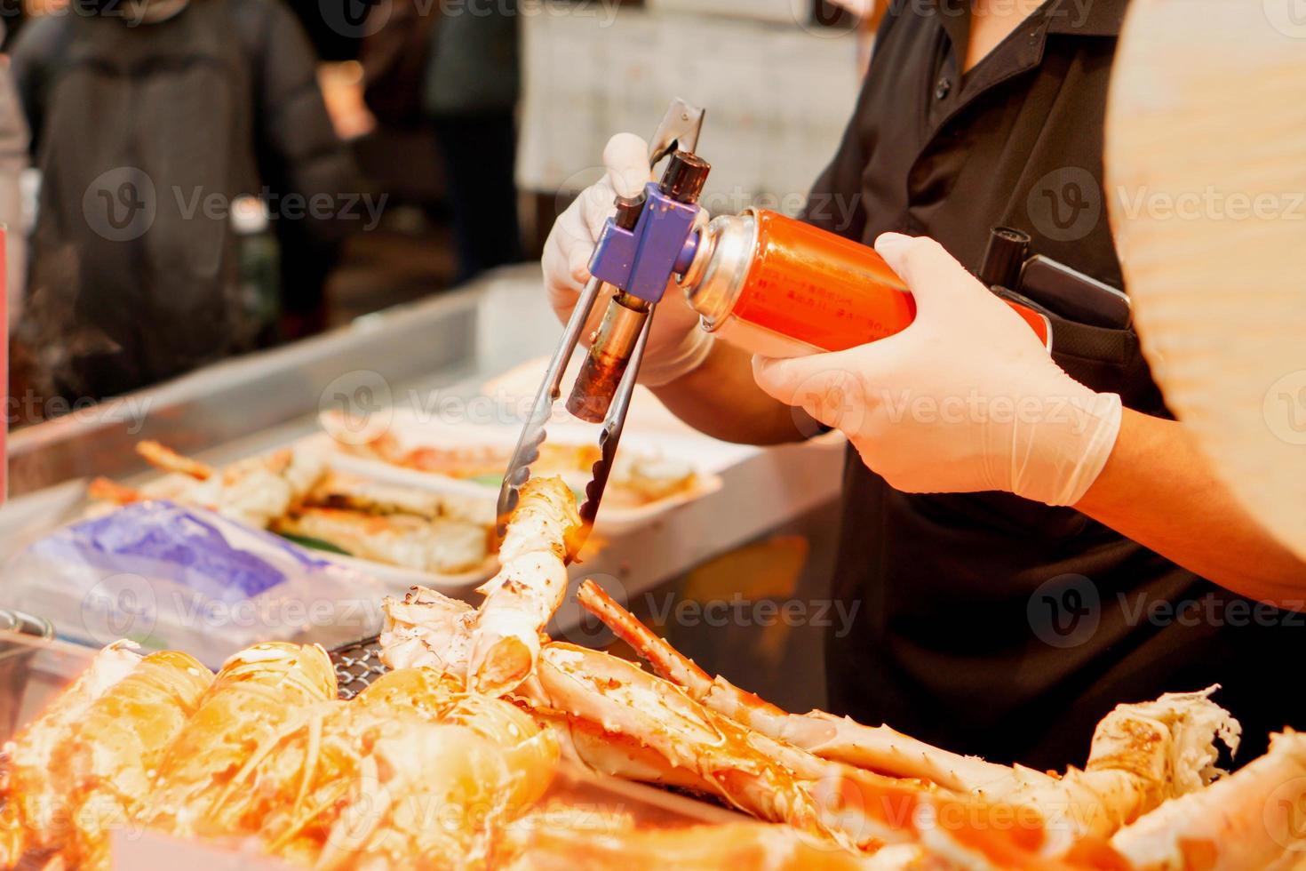 Hand of chef using burner cooking and burn King crab legs and giant prawns on stove to sale for customer at Kuromon market. King crab legs Bar-B-Q is popular among tourists who come to Japan. photo