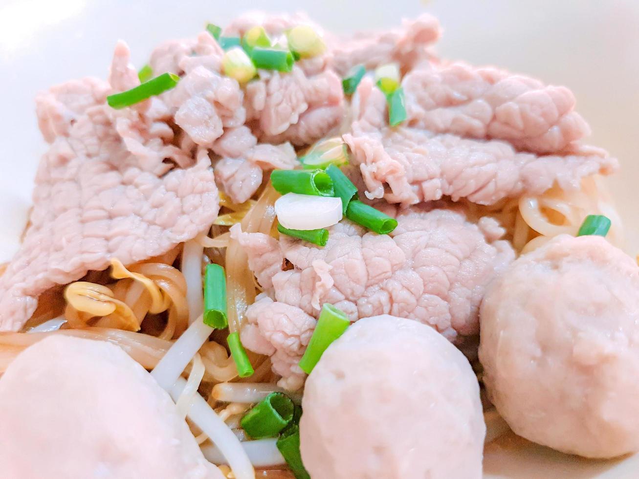 primer plano y cultivo deliciosos fideos chinos sin sopa con bolas de cerdo y un trozo de carne de cerdo en un tazón de cerámica blanca. foto