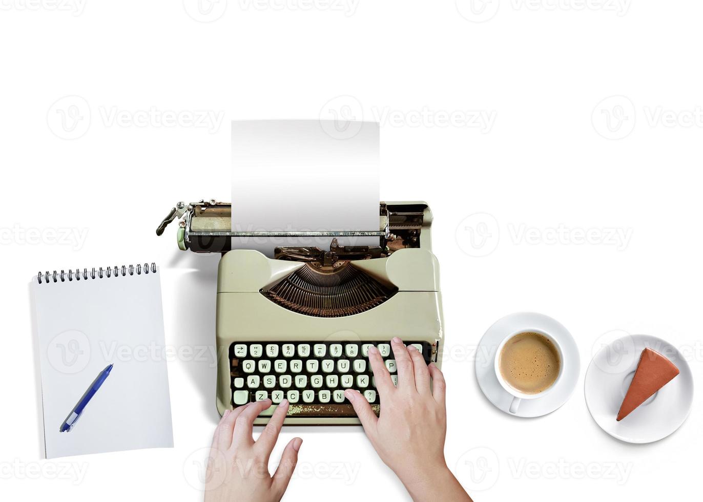 Female hand about to type on old typewriter with notebook, coffee mug, cake. Isolated on white background. Top view. photo