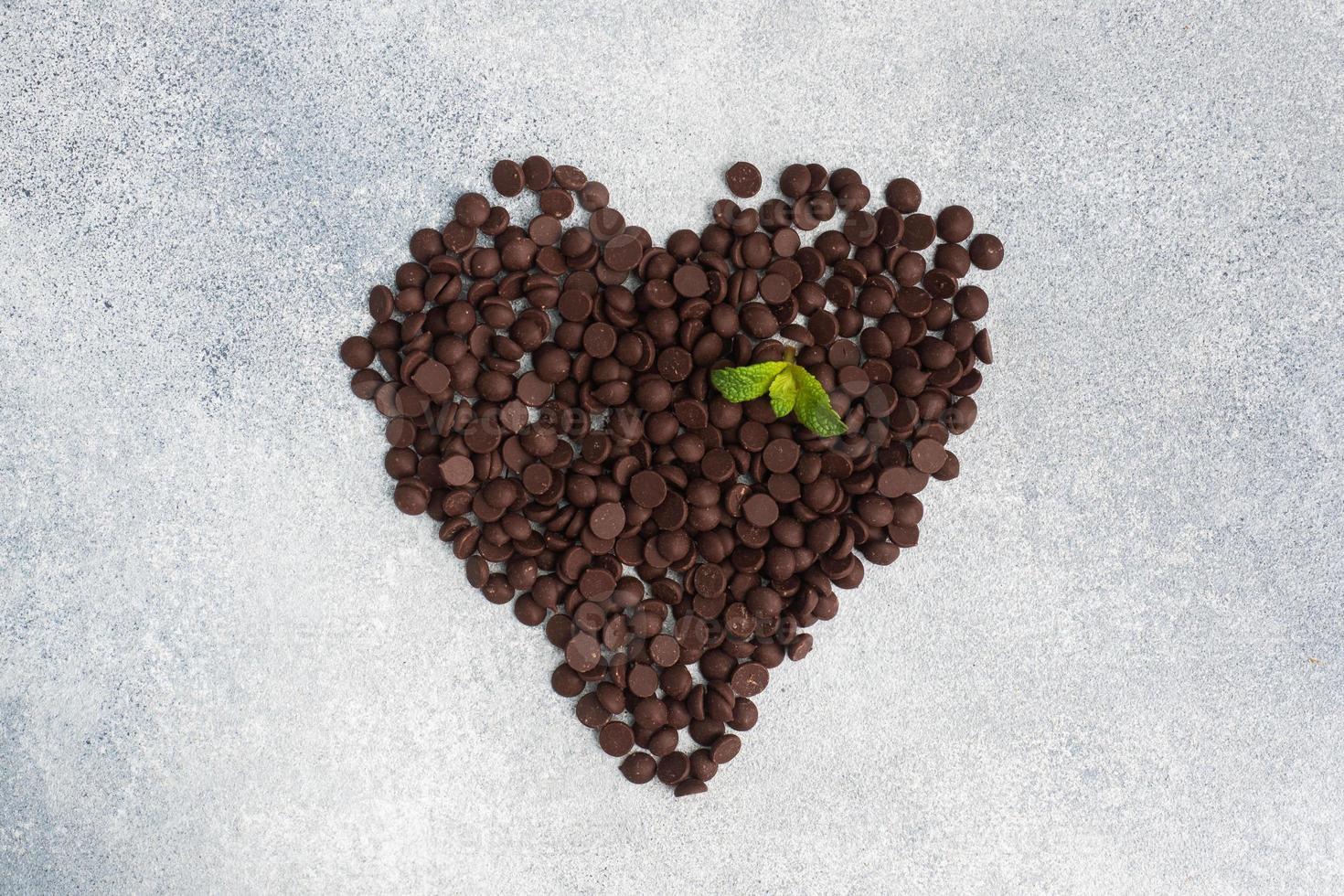 Chocolate drops laid out in the shape of a heart on a gray concrete background. Chocolate pieces for dessert decoration. photo