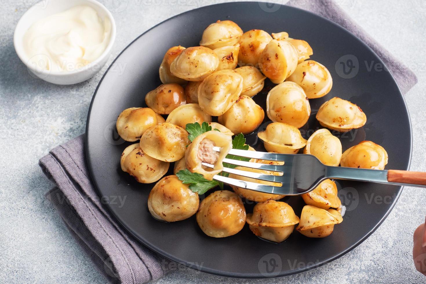 Traditional fried pelmeni, ravioli, dumplings filled with meat on black plate, russian kitchen. Gray concrete background, copy space. photo