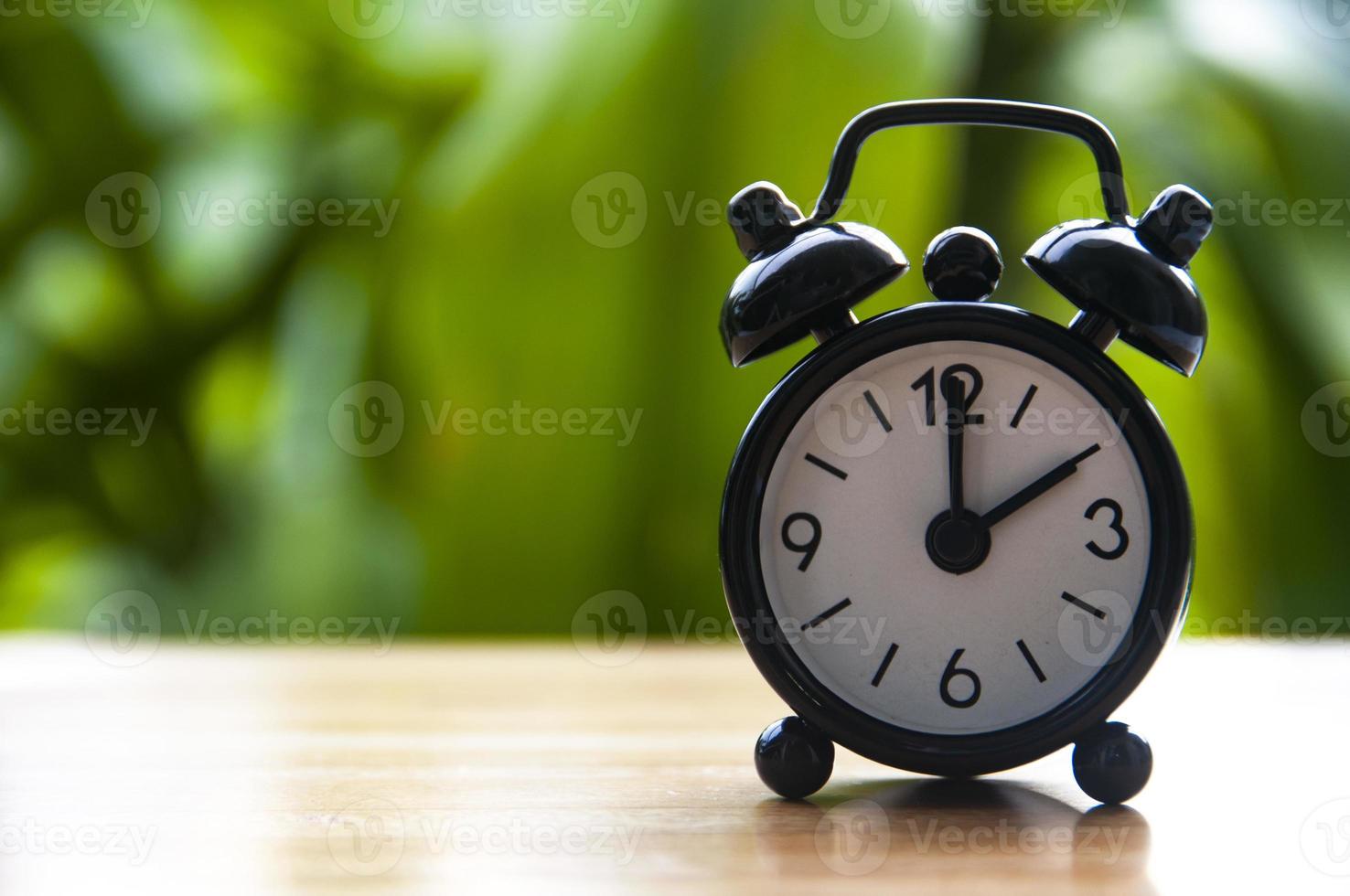 Alarm clock pointing at 2pm with blurred nature background. With customizable space for text