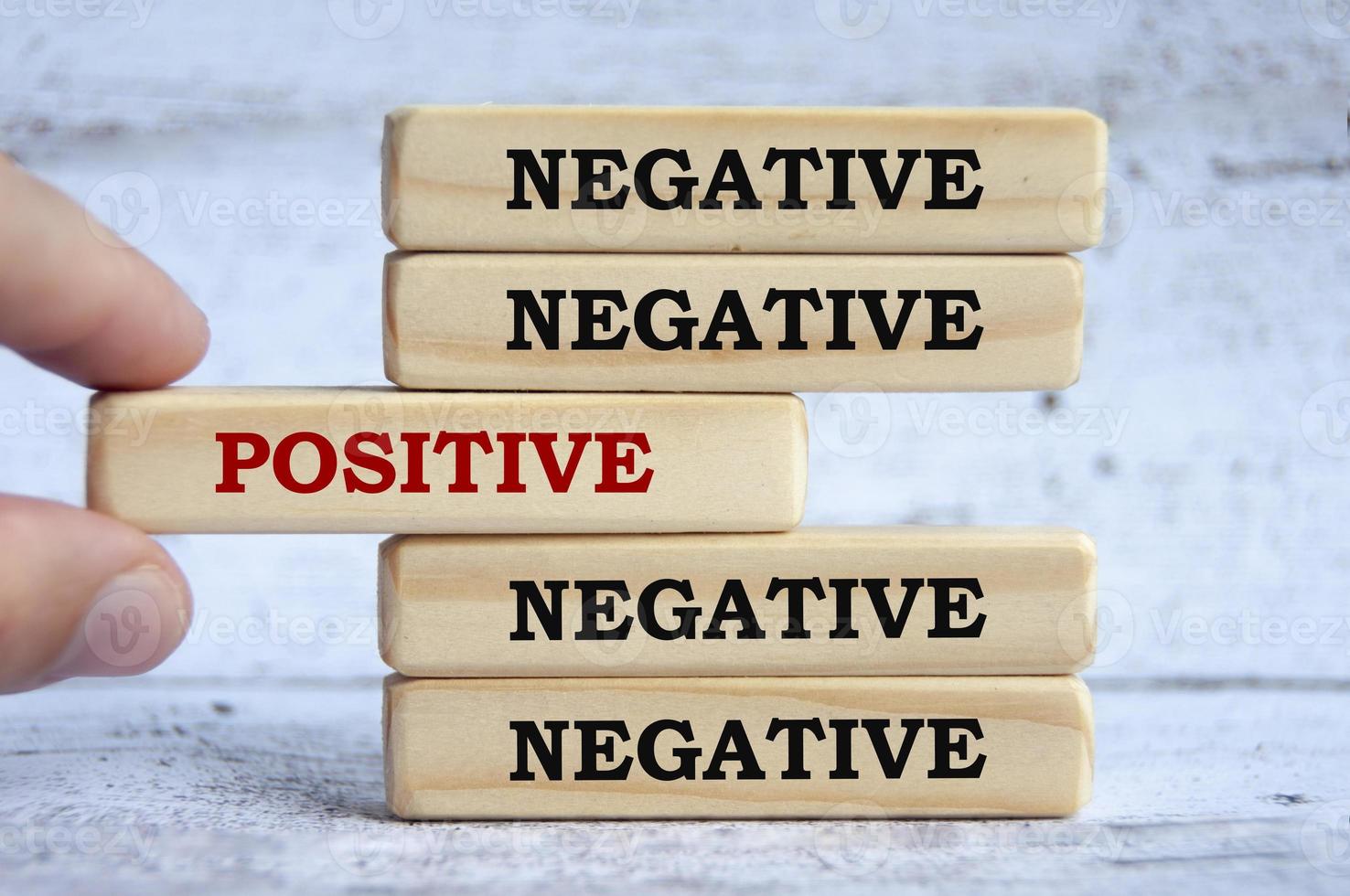Negative and positive text on wooden blocks with hand placing a wooden block in the middle. photo