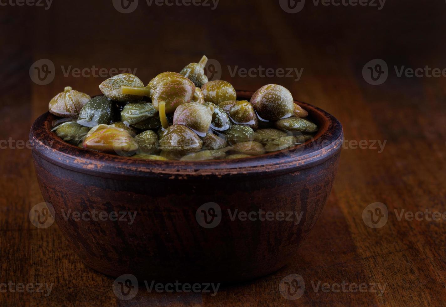 Clay bowl with capers stands on a wooden table. photo