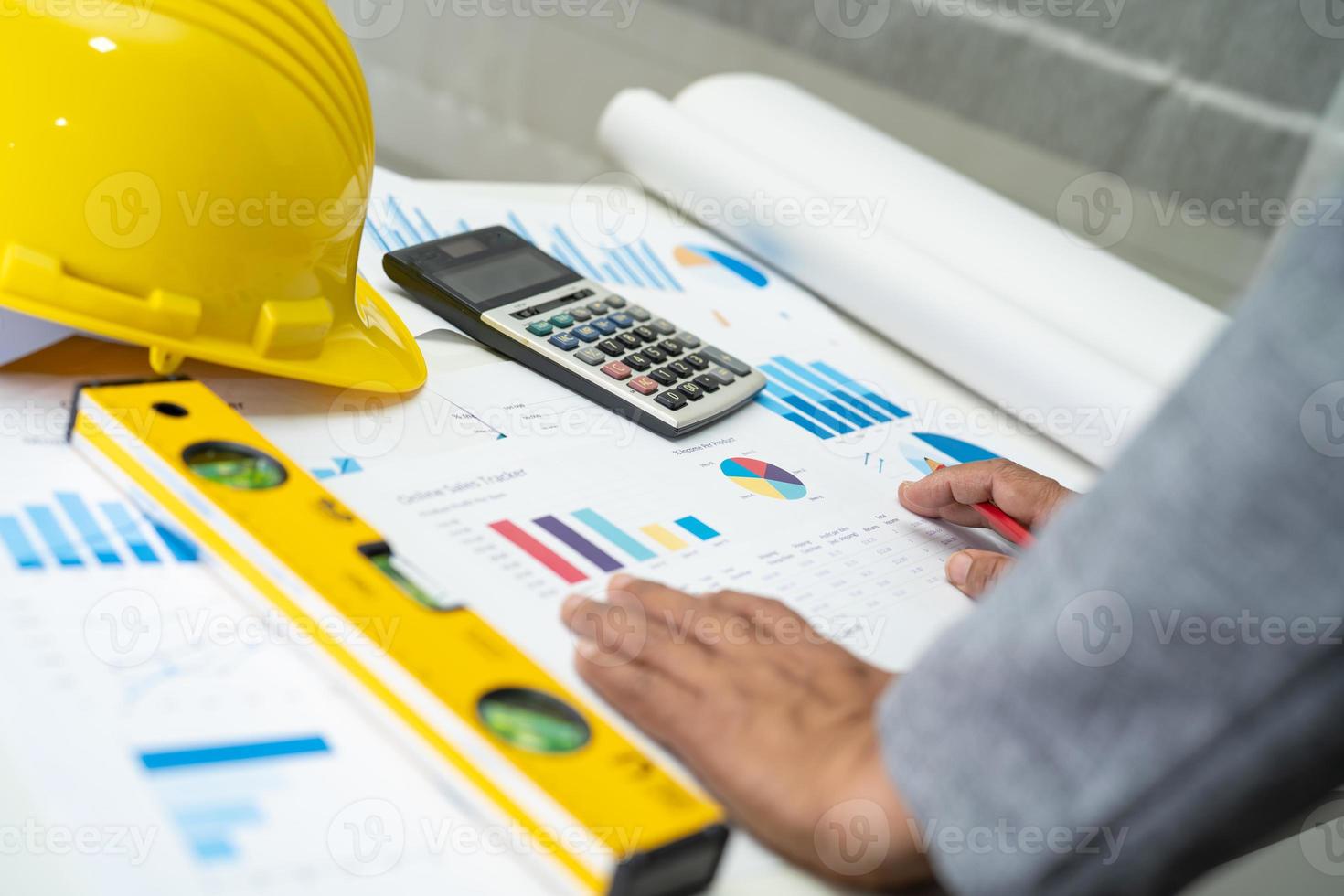 ingeniero asiático con plano de proyecto de casa arquitectónica, gráfico y casco amarillo y herramientas de construcción de ingeniería. foto