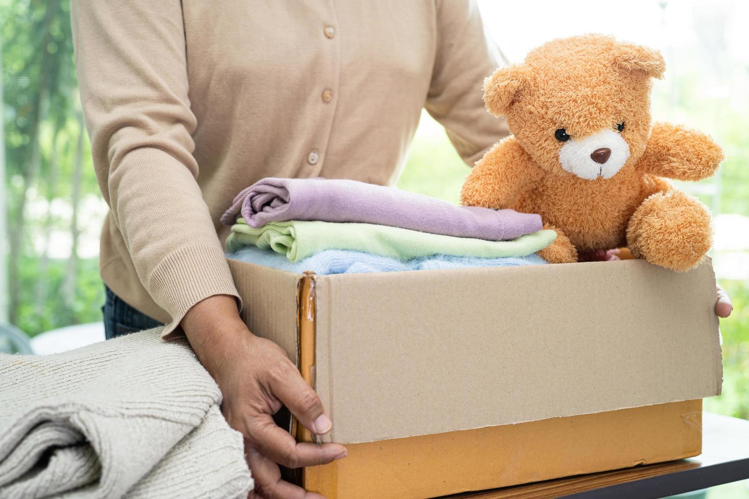 Holding clothing donation box with used clothes and doll at home to support help for poor people in the world. photo