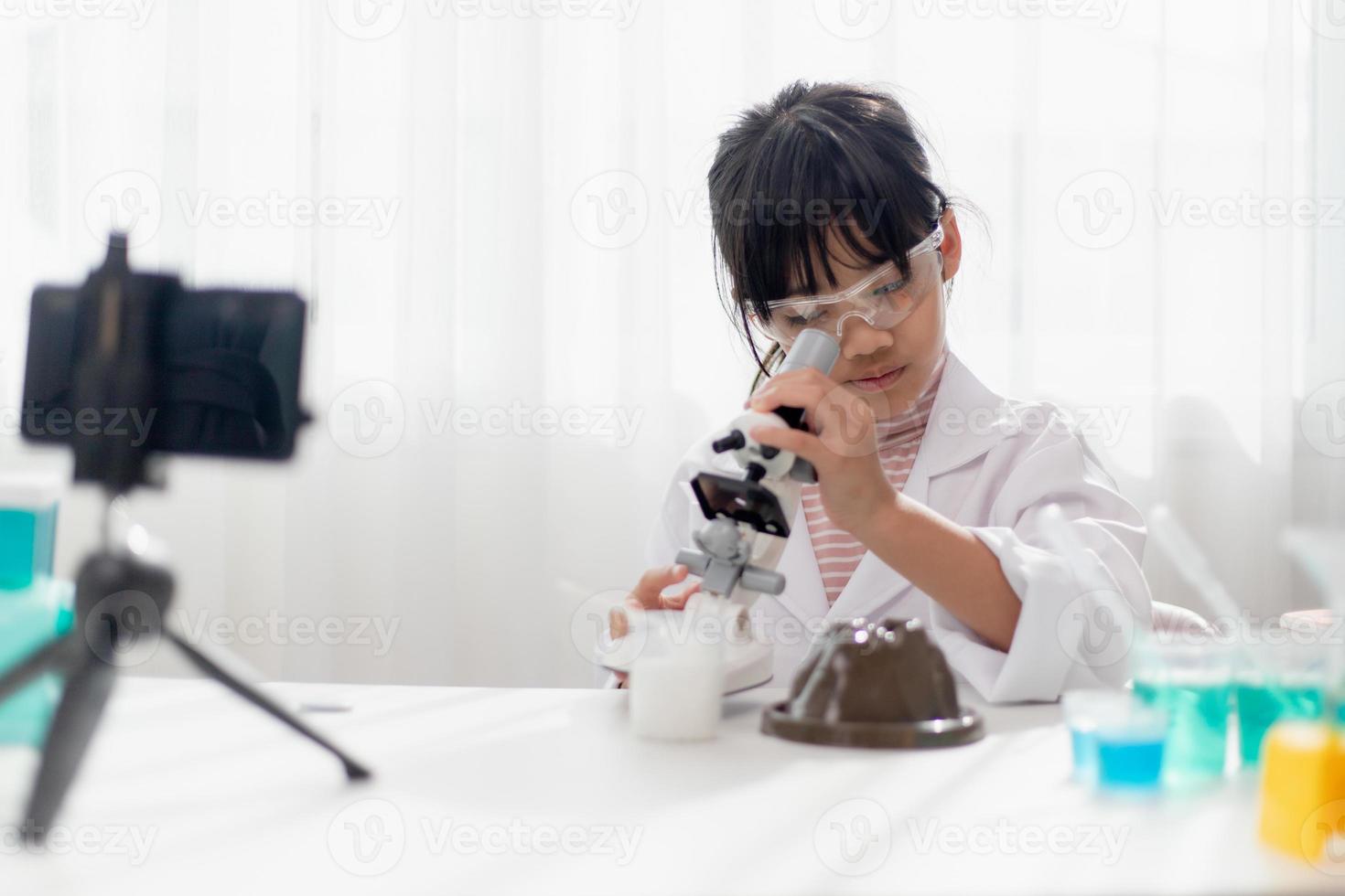 Asian school girl making easy chemistry experiments and recording a video for his followers, Young blogger kid posing in front of camera for vlog, Children make vlog for social media channel concept. photo