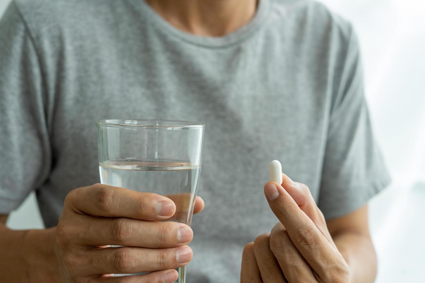 primer plano de un hombre que sostiene un suplemento dietético o un medicamento y un vaso de agua listo para tomar el medicamento. conceptos de salud de las personas. foto