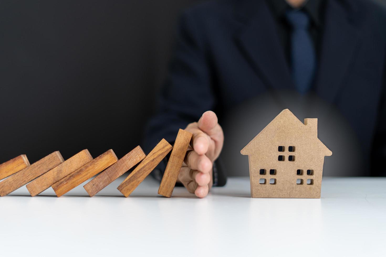 Insurance agents or family leaders are using hands to prevent Dominos from falling into the house. Prevention of external hazards. Home insurance plan photo