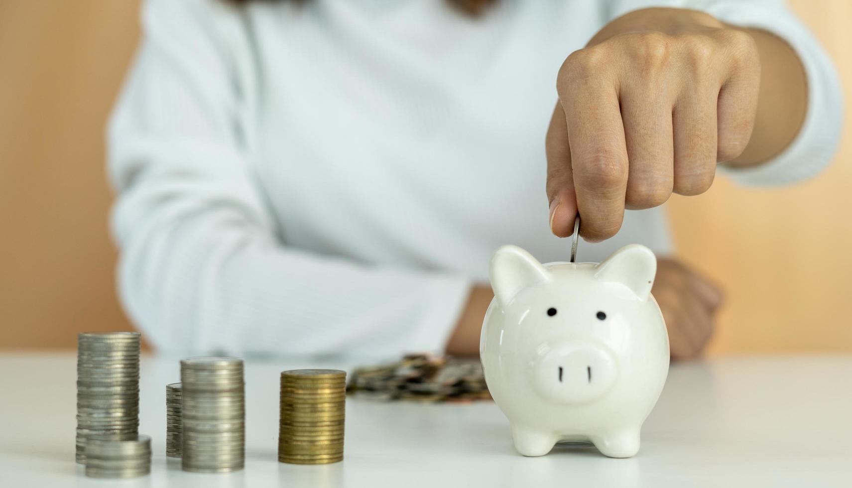 A man's hand is placing a silver coin stacked side by side with a white piggy bank. Man to collect savings as a business capital or savings money for the future. Concept saving money photo