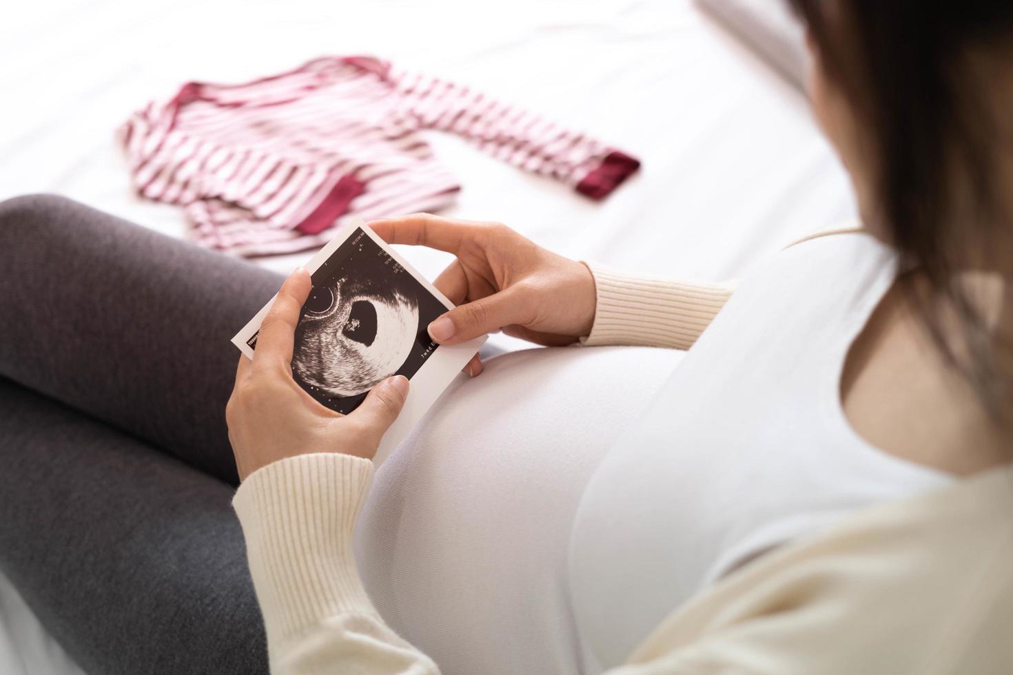 A pregnant woman is looking at an ultrasound photo of fetus. Mother gently touches the baby on stomach.Women are pregnant for 30 weeks. first love in belly and Last term pregnancy