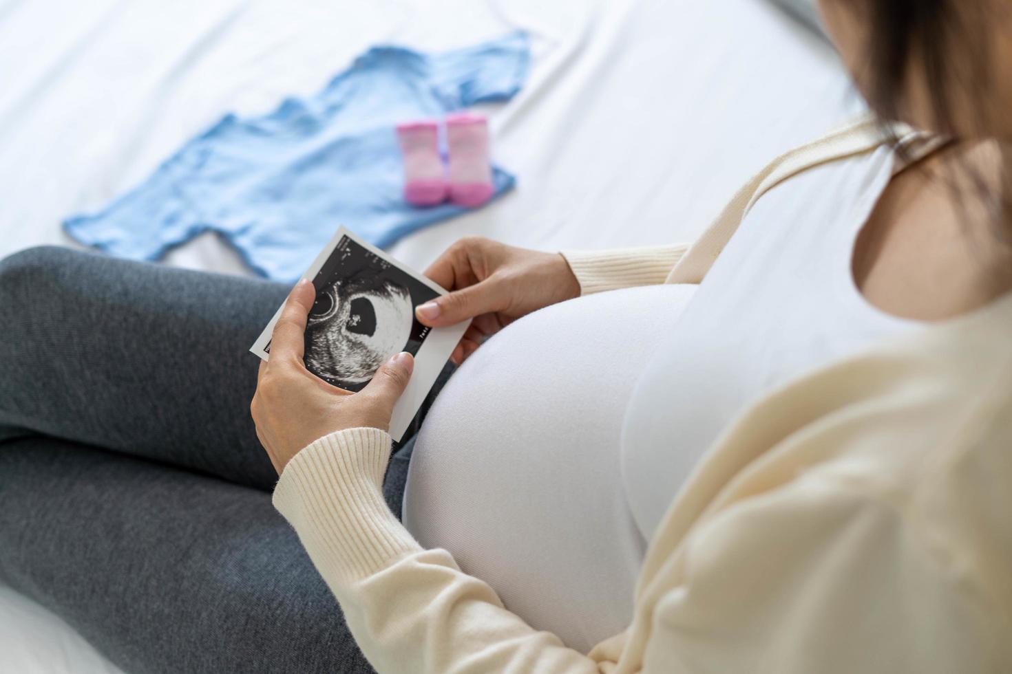 A pregnant woman is looking at an ultrasound photo of fetus. Mother gently touches the baby on stomach.Women are pregnant for 30 weeks. first love in belly and Last term pregnancy