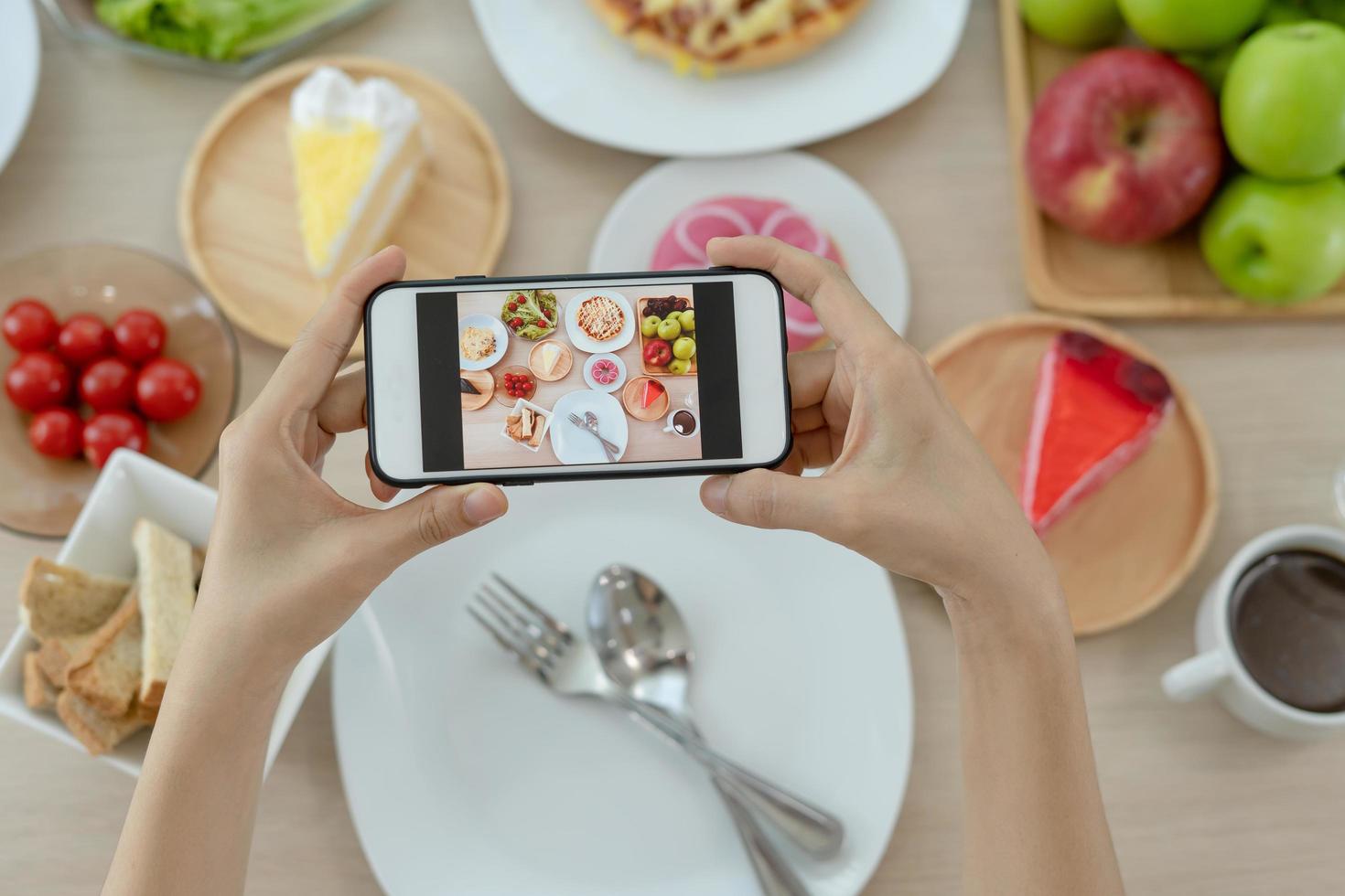 A reviewer's hand using a mobile phone to take pictures of food at a restaurant table.Take photo to write a review of the restaurant to share on the internet.