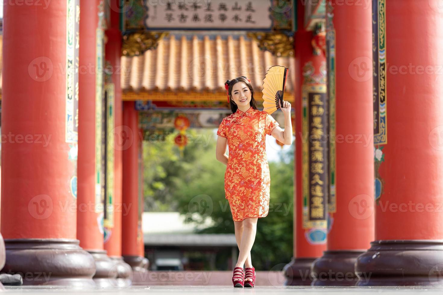 Asian woman in red cheongsam qipao dress holding paper fan while visiting the Chinese Buddhist temple during lunar new year for traditional culture concept photo