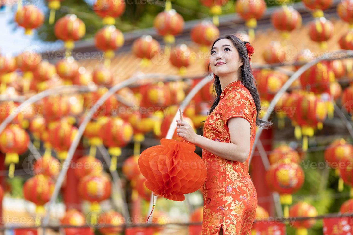 mujer asiática con vestido rojo cheongsam qipao sosteniendo una linterna mientras visita el templo budista chino durante el año nuevo lunar por el concepto de cultura tradicional foto