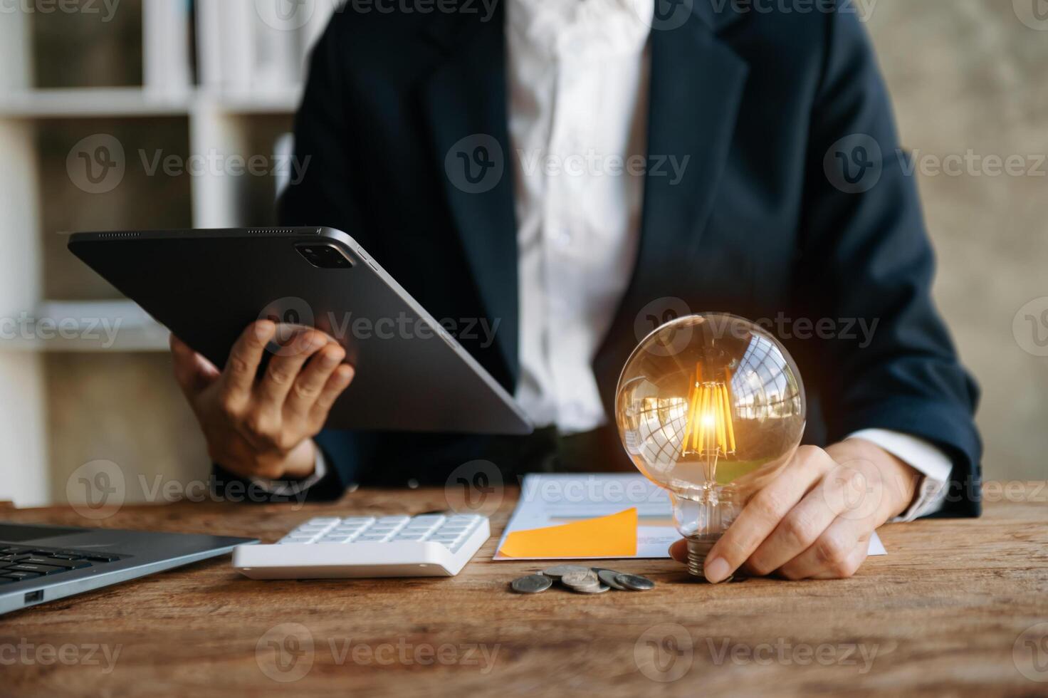 business hand holding lightbulb with using laptop computer and money stack in office. idea saving energy and accounting finance concept  in morning light photo