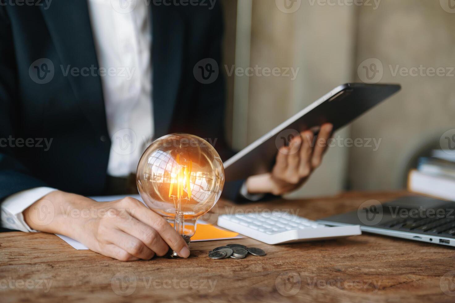 business hand holding lightbulb with using laptop computer and money stack in office. idea saving energy and accounting finance concept  in morning light photo