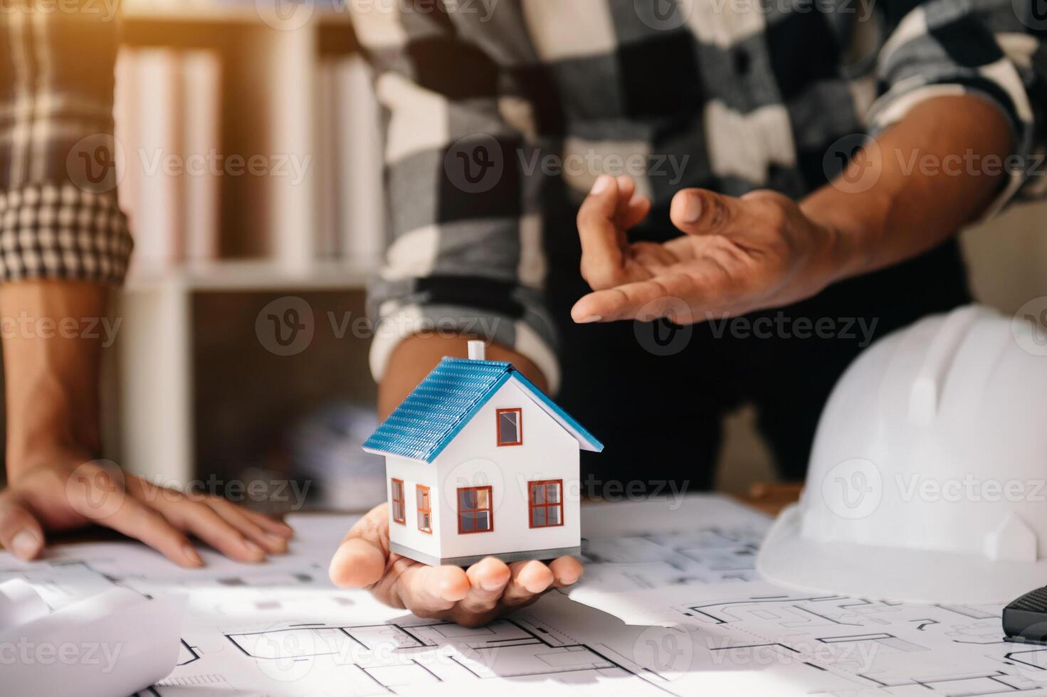 Professional architect, engineer or interior reviewing blueprint on workplace desk behind house model in office center photo