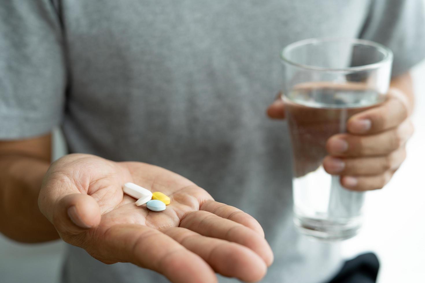 primer plano de un hombre que sostiene un suplemento dietético o un medicamento y un vaso de agua listo para tomar el medicamento. conceptos de salud de las personas. foto