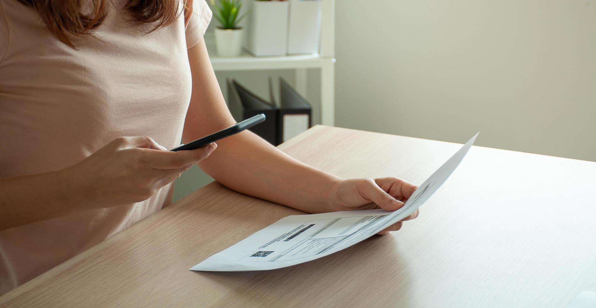 woman use phone to scan barcode or QR codes to pay credit card bill after receiving document invoice online. payment, receive, paying electricity, digital payments without money, technology, photo