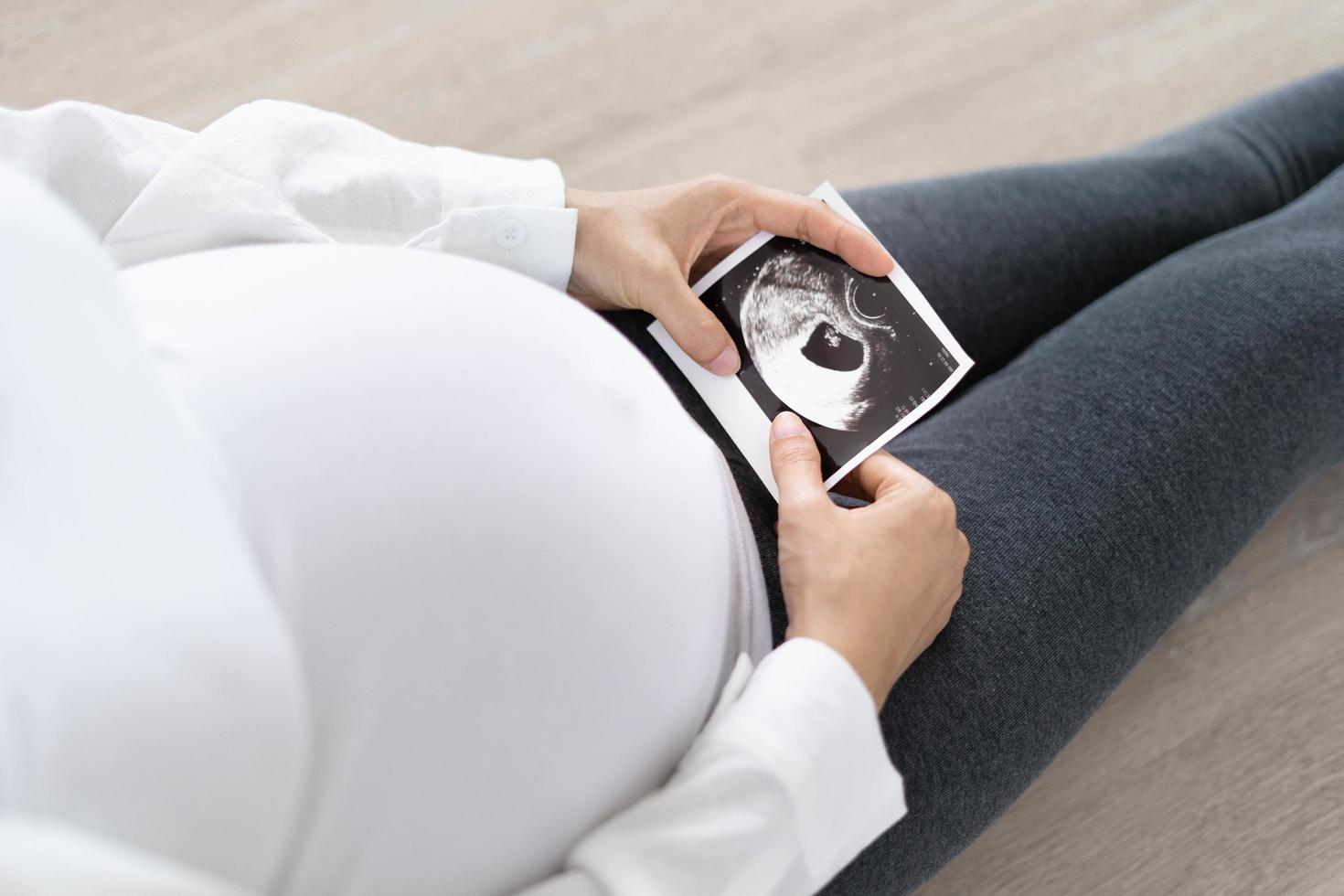 A pregnant woman is looking at an ultrasound photo of fetus. Mother gently touches the baby on stomach.Women are pregnant for 30 weeks. first love in belly and Last term pregnancy