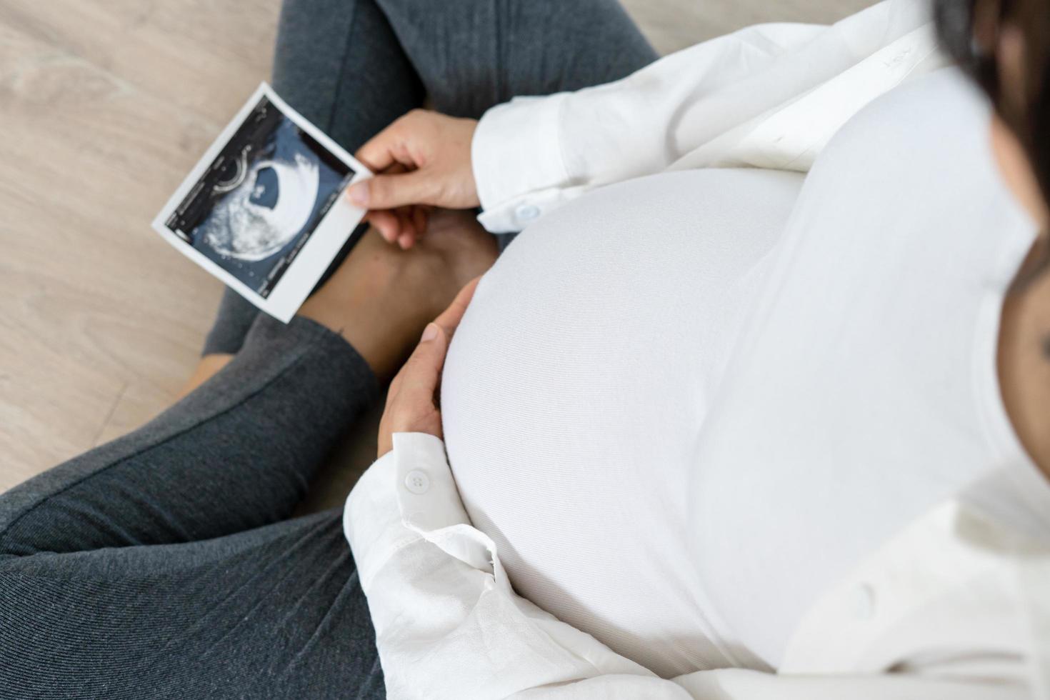 A pregnant woman is looking at an ultrasound photo of fetus. Mother gently touches the baby on stomach.Women are pregnant for 30 weeks. first love in belly and Last term pregnancy