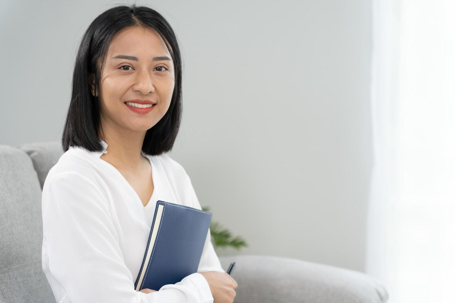 Asian businesswoman smiling and holding a book in office. Beautiful and good looking Asian woman sits on the sofa. female portraits. photo