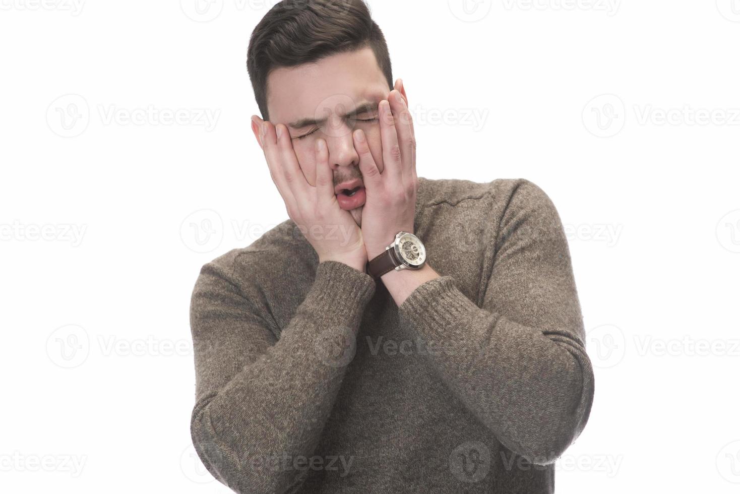 Stop that loud noise. Standing plain young man sad and depressed suffering sorrow and pain screaming desperate with hands on face against  white background. Sadness emotion concept photo