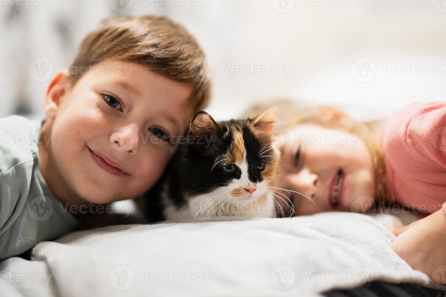Brother and sister with kitty cat lying on the sofa. Children's love for pets. photo