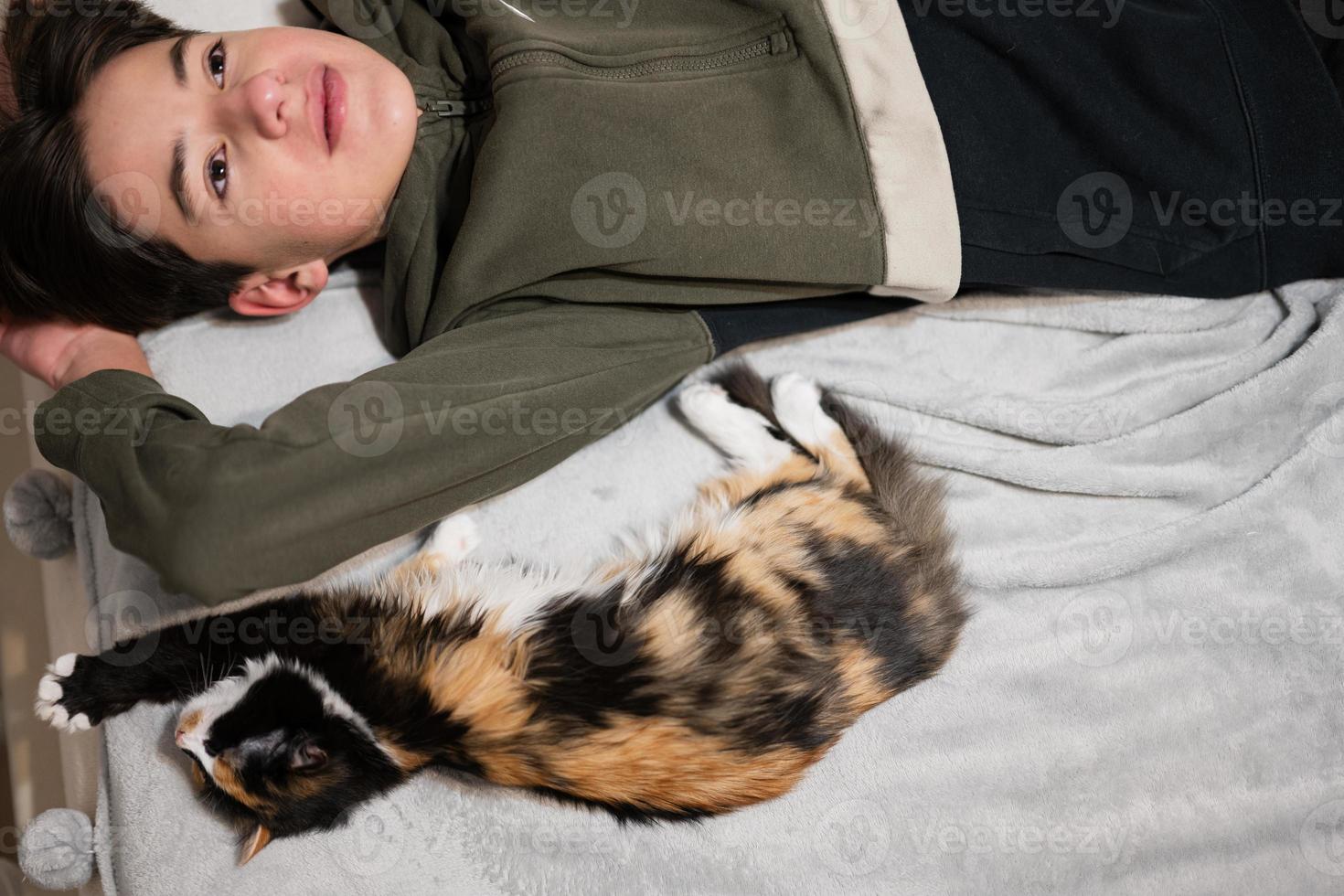 Teenager boy with kitty lying on the sofa. Children's love for pets. photo