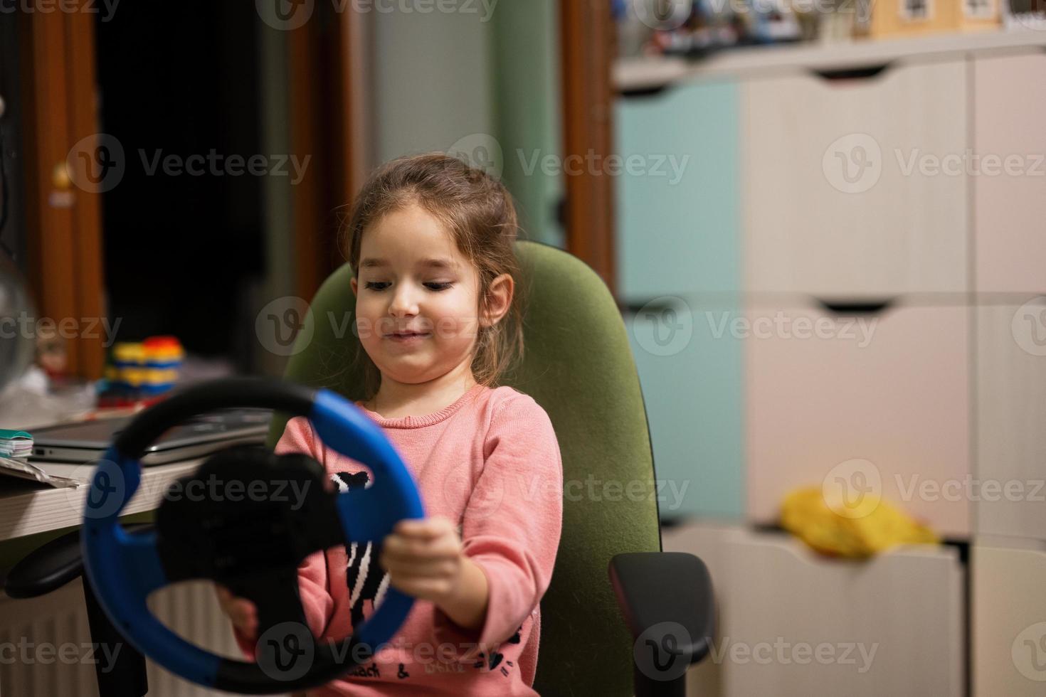 Girl sitting on chair with a child's steering wheel in her hands in children's room. photo